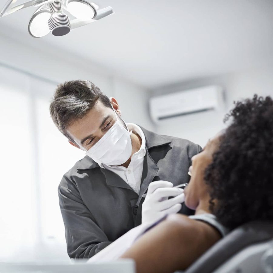 Male dentist examining teeth of patient on chair. Woman is visiting doctor for dental checkup. They are in clinic.