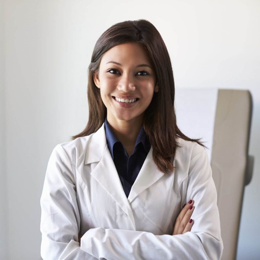 Portrait Of Female Doctor Wearing White Coat In Exam Room